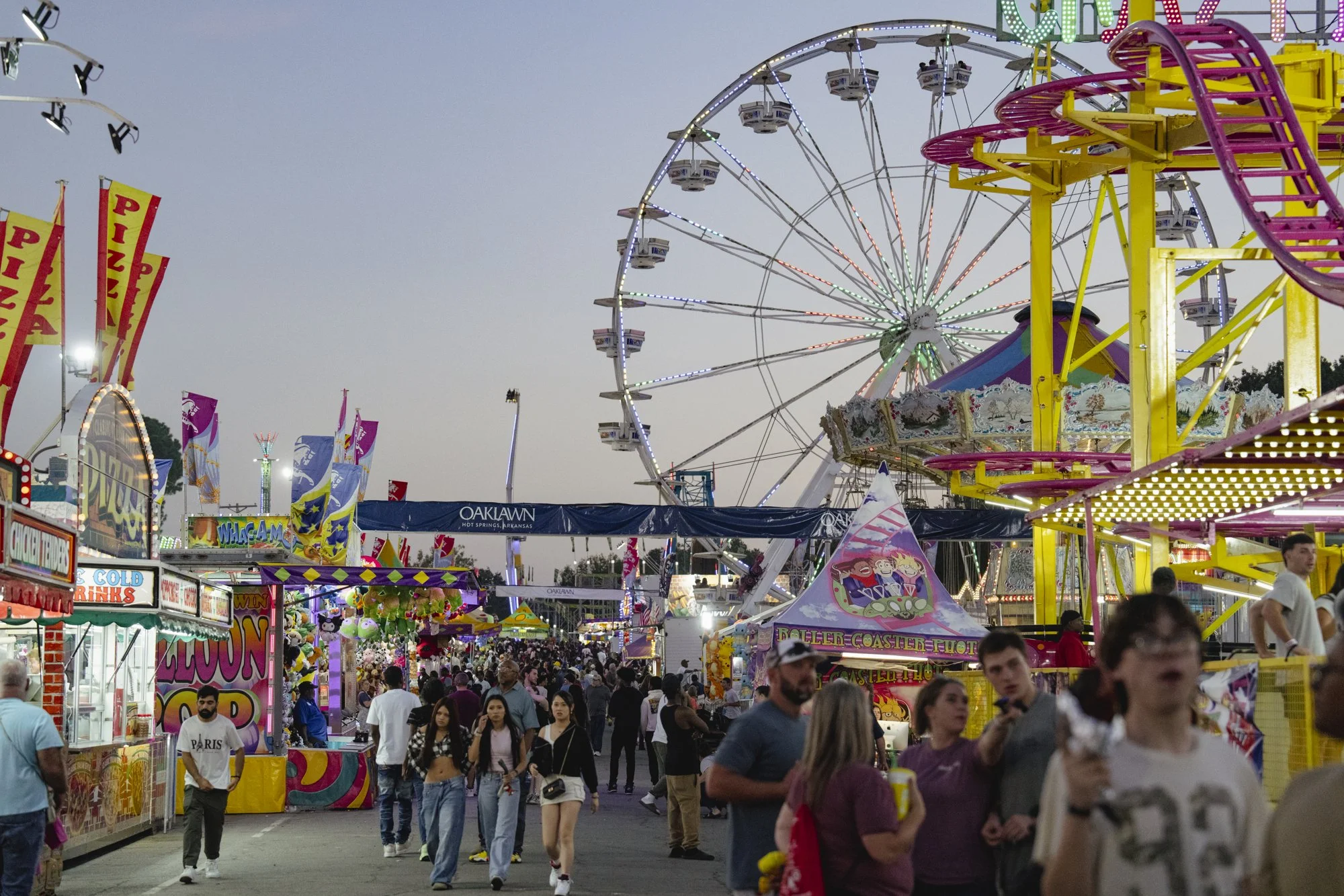 Crowds, food stalls, a Ferris wheel, and midway rides at the Arkansas State Fair